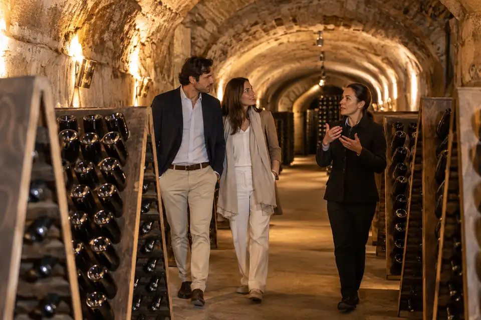 Visiteurs dans une cave de Champagne voûtée avec des bouteilles sur des pupitres en bois