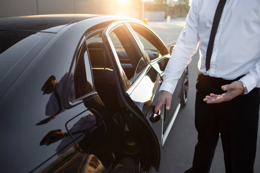Chauffeur près de la porte arrière ouverte d’une berline noire