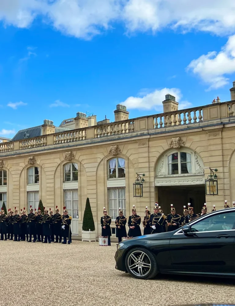 Black Mercedes in a palace courtyard beside a ceremonial formation.