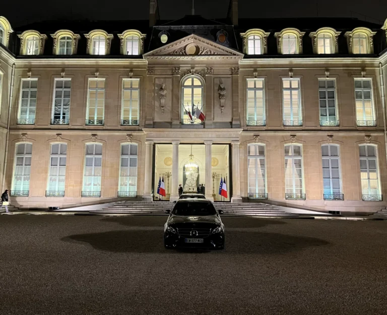Black Mercedes outside an illuminated palace at night.